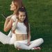 A mother and daughter in white activewear sitting on grass, enjoying a sunny day outdoors.